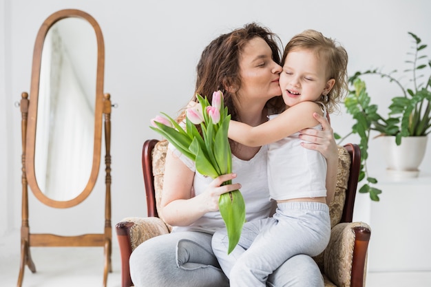 Foto gratuita la bella madre che bacia al suo bambino a casa che tiene il mazzo di fiori del tulipano