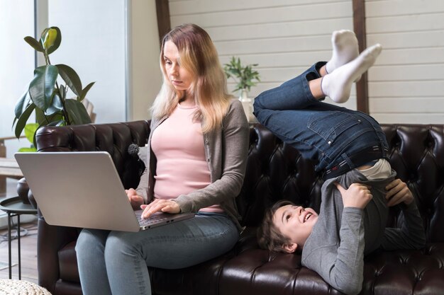 Beautiful mother working next to son on the couch