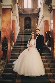 Красивые молодожены обнимаются на лестнице старинного дома. свадебный портрет стильного жениха и молодой невесты внутри.
