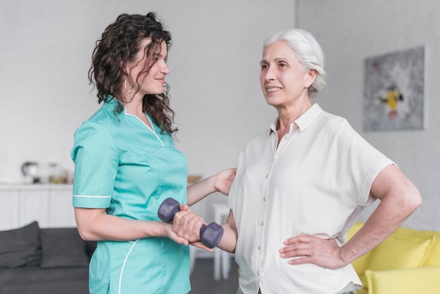 Beautiful old lady is doing exercise with dumbbell with the help of physiotherapist