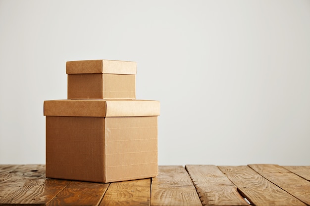 Beautiful old uneven wooden table with two blank similar cardboard boxes with covers against white wall background