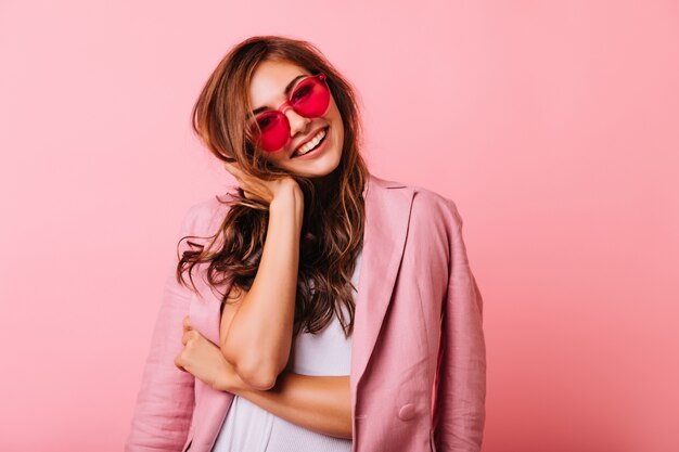 Bella ragazza ottimista che tocca i suoi capelli allo zenzero. ritratto dell'interno del modello femminile bianco beato isolato su roseo.