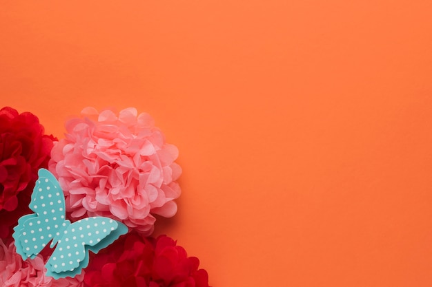 Free photo beautiful origami paper flowers and polka dotted blue butterfly on orange backdrop