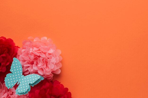 Beautiful origami paper flowers and polka dotted blue butterfly on orange backdrop