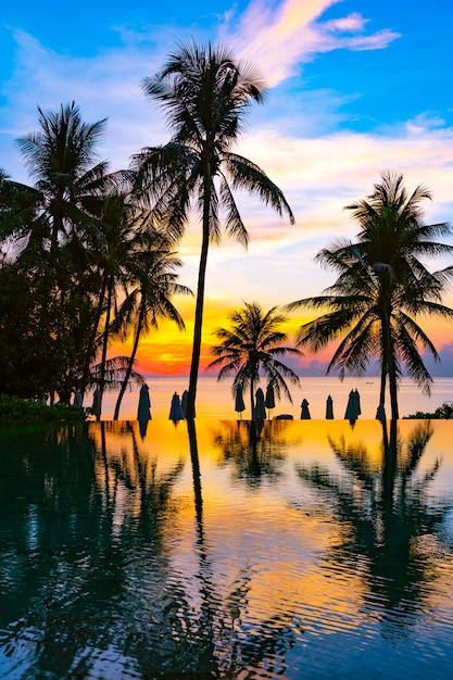 Beautiful outdoor nature landscape with sea ocean and coconut palm tree around swimming pool at sunrsie or sunset