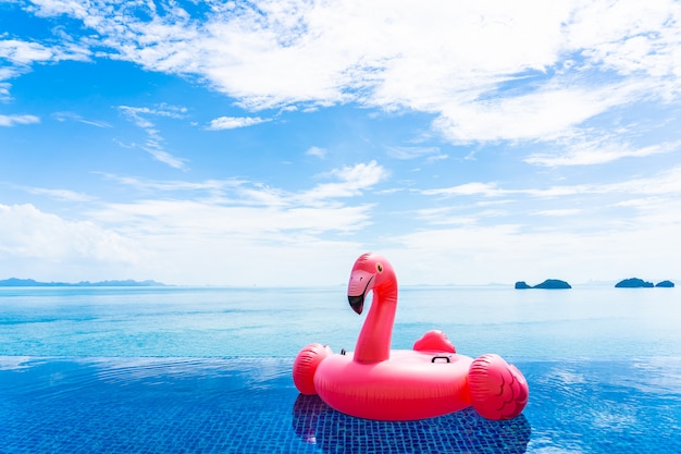 Beautiful outdoor swimming pool in hotel resort with flamingo float around sea ocean white cloud on blue sky