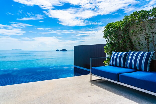 Beautiful outdoor swimming pool with sea ocean on white cloud blue sky 