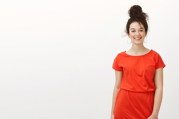 Beautiful outgoing caucasian female in red dress with combed hair, smiling broadly