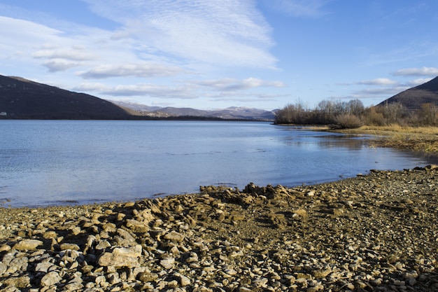 Beautiful panoramic shot of a stony serene shore under a blue cloudy sky