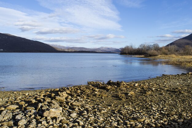 Beautiful panoramic shot of a stony serene shore under a blue cloudy sky