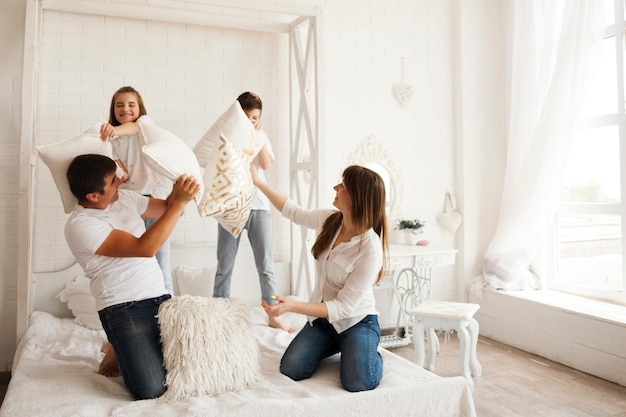 침실에서 침대에 베개 싸움을하는 그들의 아이와 아름다운 부모