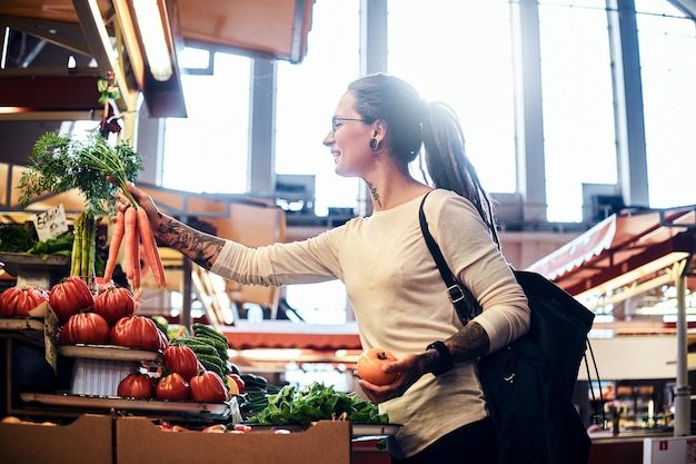 Beautiful pensive girl in glasses is buying fresh carrots at local farmer's market.