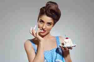 Free photo beautiful pin-up woman eating cake at studio