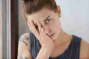 Free photo beautiful portrait of bored female resting half of her face on her palm. attractive girl with brown hair and blue eyes getting tired of wonky conversation, trying to hide from dull talk under her arm.