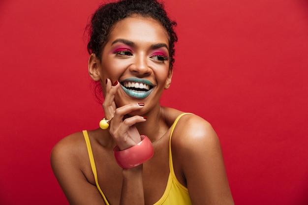 Foto gratuita bello ritratto del modello femminile afroamericano felice in camicia gialla che sorride e che posa sulla macchina fotografica, isolato sopra la parete rossa