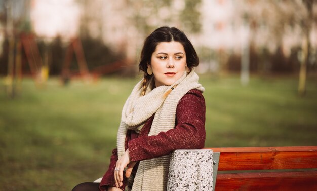 Beautiful portrait of a pretty brunette girl smiling, sitting on the bench  in the park