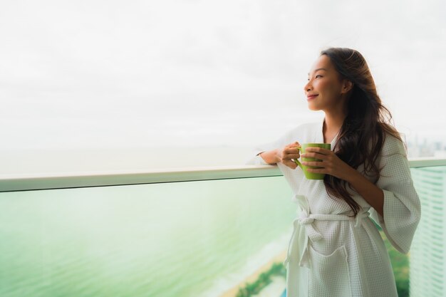 Free Photo beautiful portrait young asian women holding coffee cup at outdoor balcony with sea ocean view