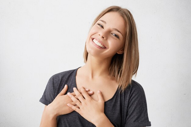 Beautiful positive friendly-looking young mixed race woman with lovely sincere smile feeling thankful and grateful, showing her heart filled with love and gratitude with hands on her breast