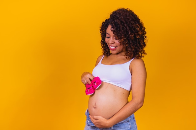 黄色の背景にピンクのスリッパと美しい妊娠中の母親 Premium写真