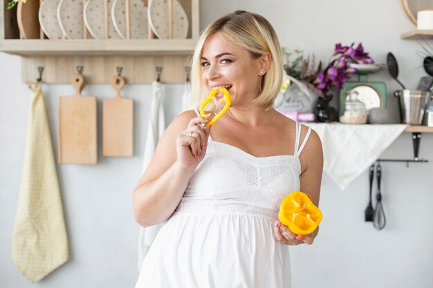 Beautiful pregnant woman eating yellow pepper