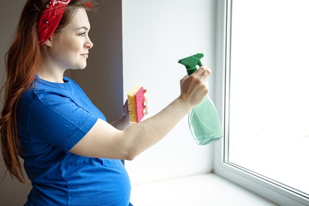 A beautiful pregnant woman in the last months of pregnancy is engaged in cleaning and washes the windows.