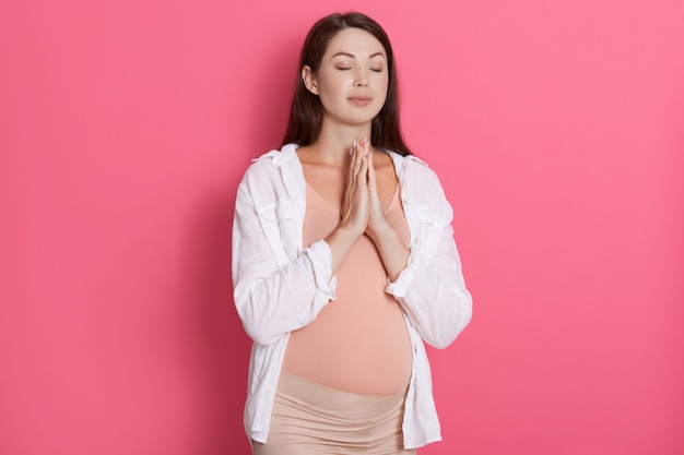 Beautiful pregnant woman meditates isolated over pink