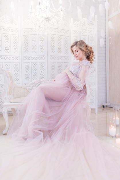 Beautiful pregnant woman in rich pink dress holds hands on her belly posing