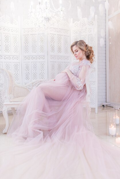 풍부한 핑크 드레스에 아름 다운 임신 한 여자는 그녀의 배꼽 포즈에 손을 보유하고