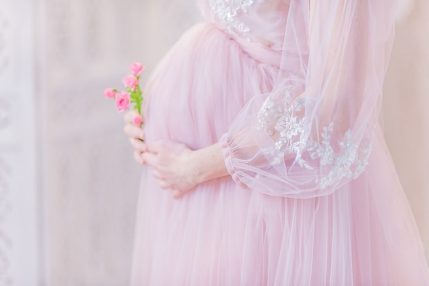풍부한 핑크 드레스에 아름 다운 임신 한 여자는 그녀의 배꼽 포즈에 손을 보유하고