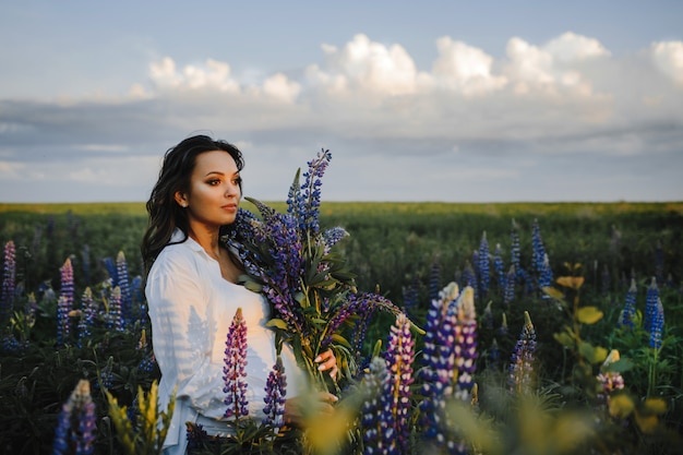 Free photo beautiful pregnant woman stands among field of lupines on sky