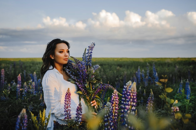Beautiful pregnant woman stands among field of lupines on sky 