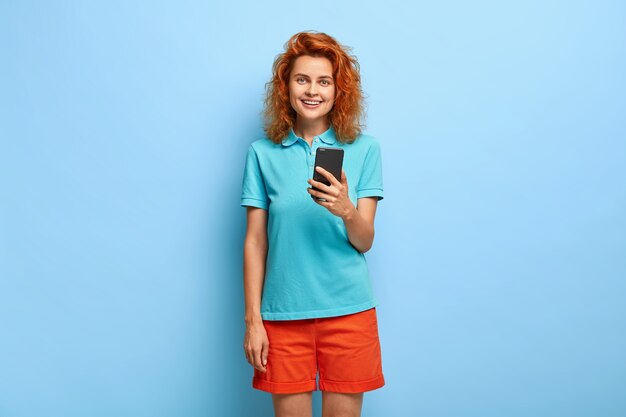 Beautiful red haired teenage girl uses smartphone device, installs new application