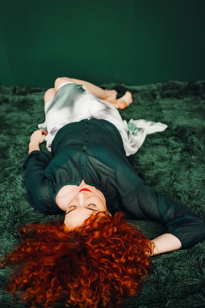 Beautiful red-haired woman lies on a green blanket