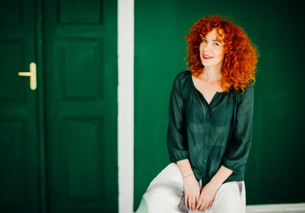 Foto gratuita bella donna dai capelli rossi sitts su uno sfondo verde