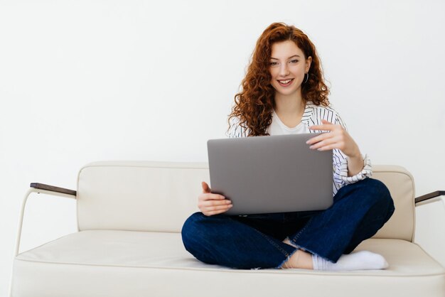 편안한 회색 소파에 앉아 노트북을 사용하여 온라인으로 일하는 아름다운 redhaired 여성