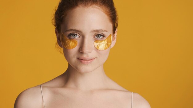 Free photo beautiful redhead girl in gold eye patches confidently looking in camera over colorful background