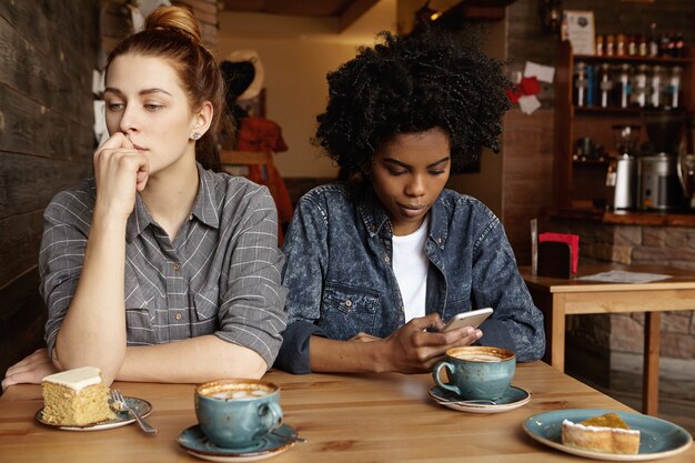 彼女のインターネット中毒のガールフレンドと昼食時にカフェに座って心配そうな表情を持つ美しい赤毛の女の子