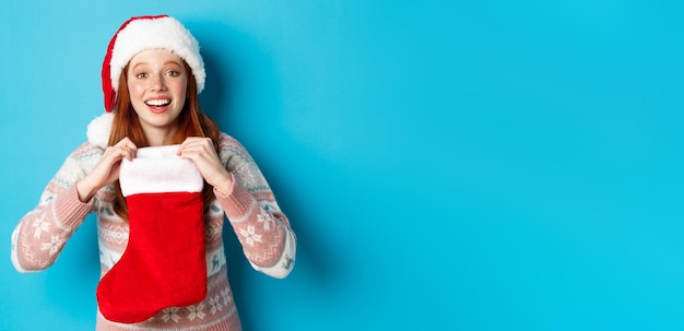 Free photo beautiful redhead girl in santa hat open christmas stocking and looking surprised receiving xmas gif