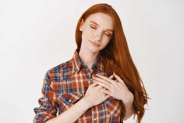 Free photo beautiful redhead woman standing with closed eyes and hands on heart feeling touched dreaming about something standing over white background