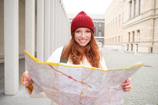 無料写真 市内地図を持つ美しい赤毛の女性観光客は、歩き回って観光の歴史的建造物を探索します
