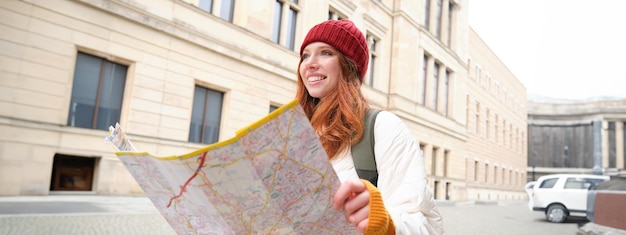 Free photo beautiful redhead woman tourist with city map explores sightseeing historical landmark walking