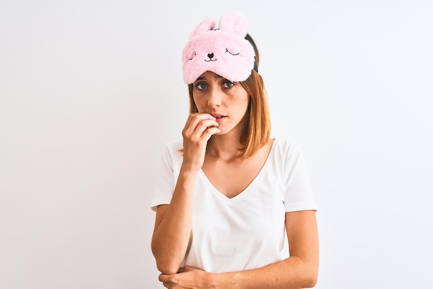 Beautiful redhead woman wearing sleeping mask over isolated background looking stressed and nervous with hands on mouth biting nails Anxiety problem