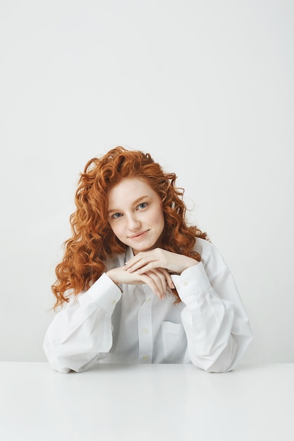 Foto gratuita donna bella rossa con seduta sorridente di capelli ricci al tavolo.