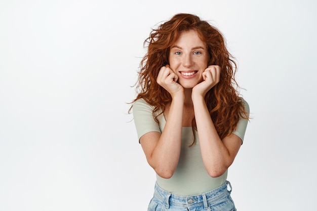 Beautiful redhead woman with natural long curly hair and freckles clean face without makeup smiling and gazing at camera showing cute face white background