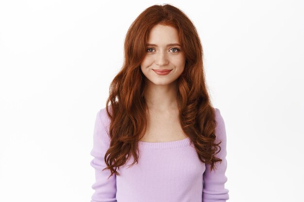 Beautiful romantic girl with red hair, purple elegant blouse, smiling sweet and tender at camera, standing against white background