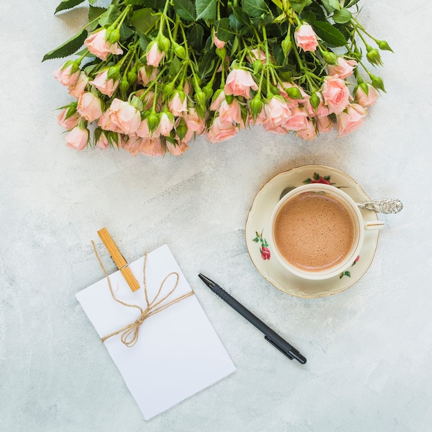 Красивые розы; почки; поздравительная открытка; ручка и чашка кофе на бетонном фоне