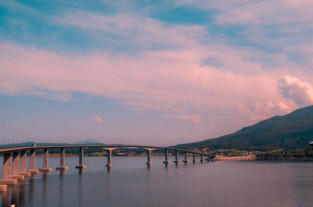 Beautiful scenery of a concrete bridge over the lake near high mountains during sunset in Norway