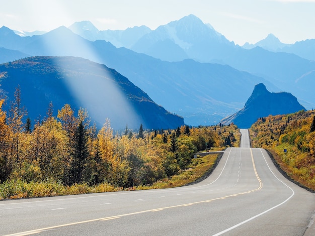 Beautiful scenery of a pathway surrounded by high rocky mountains and greenery under a cloudy sky