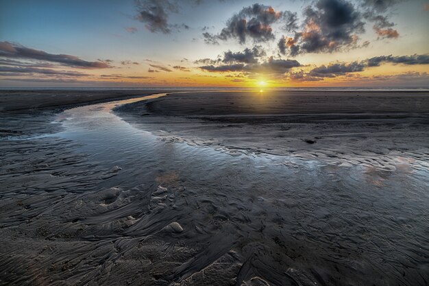 Beautiful scenery of the sunset reflected in a mudflat under the cloudy sky