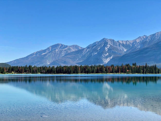 Beautiful scenery of trees and high snowy mountains reflecting in the clear lake